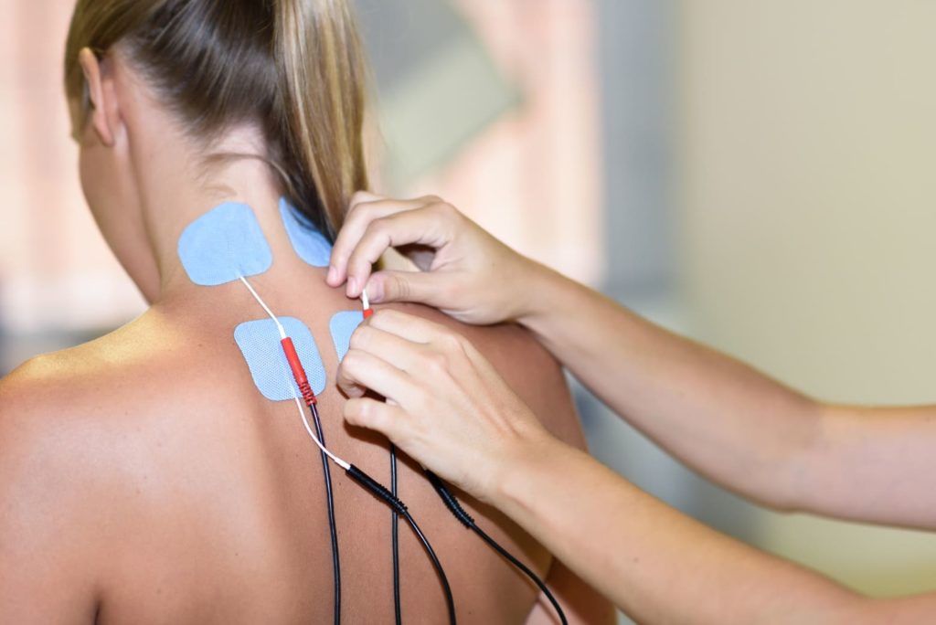 Manos de mujer insertan electrodos a mujer para realizar el tratamineto con chaleco de electroestimulación
